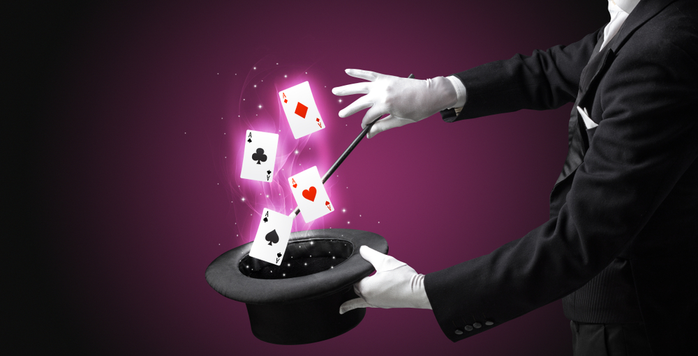 Magician with white gloves conjuring playing cards from a cylinder with magic wand