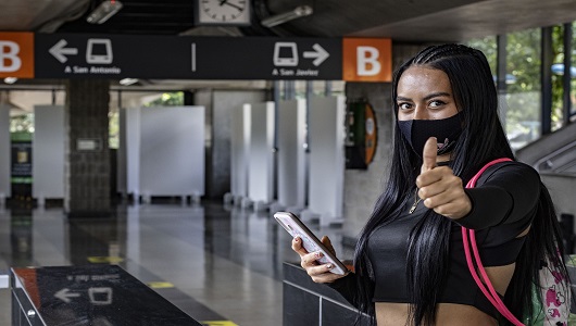 Una joven en una estación de la línea B del Metro, con el dedo arriba recomendando el uso del tapabocas.